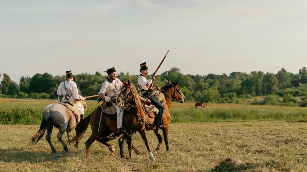 Reenactment of soldiers on horseback in a green field, evoking a historical era.