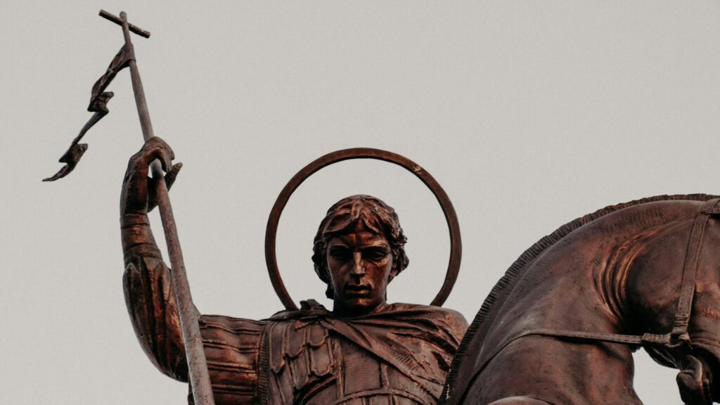 Close-up of a bronze equestrian statue representing a saint with a halo and flag.