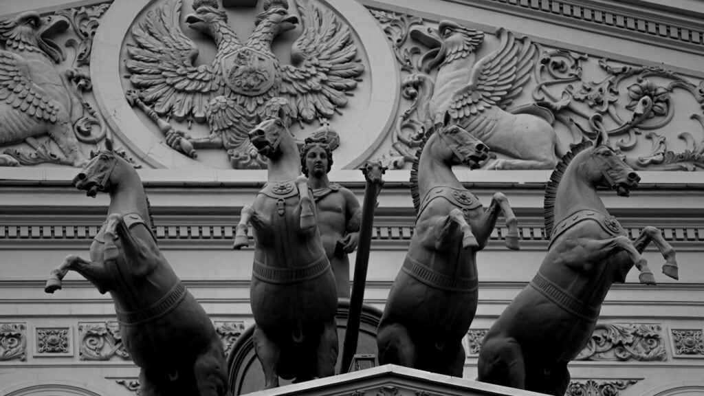 Black and white photo of elaborate horse sculptures and ornate relief on a historical building facade.