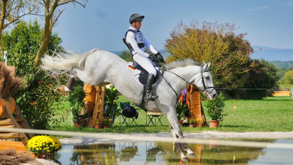 Dynamic shot of a horse and rider jumping over a water obstacle in Switzerland.