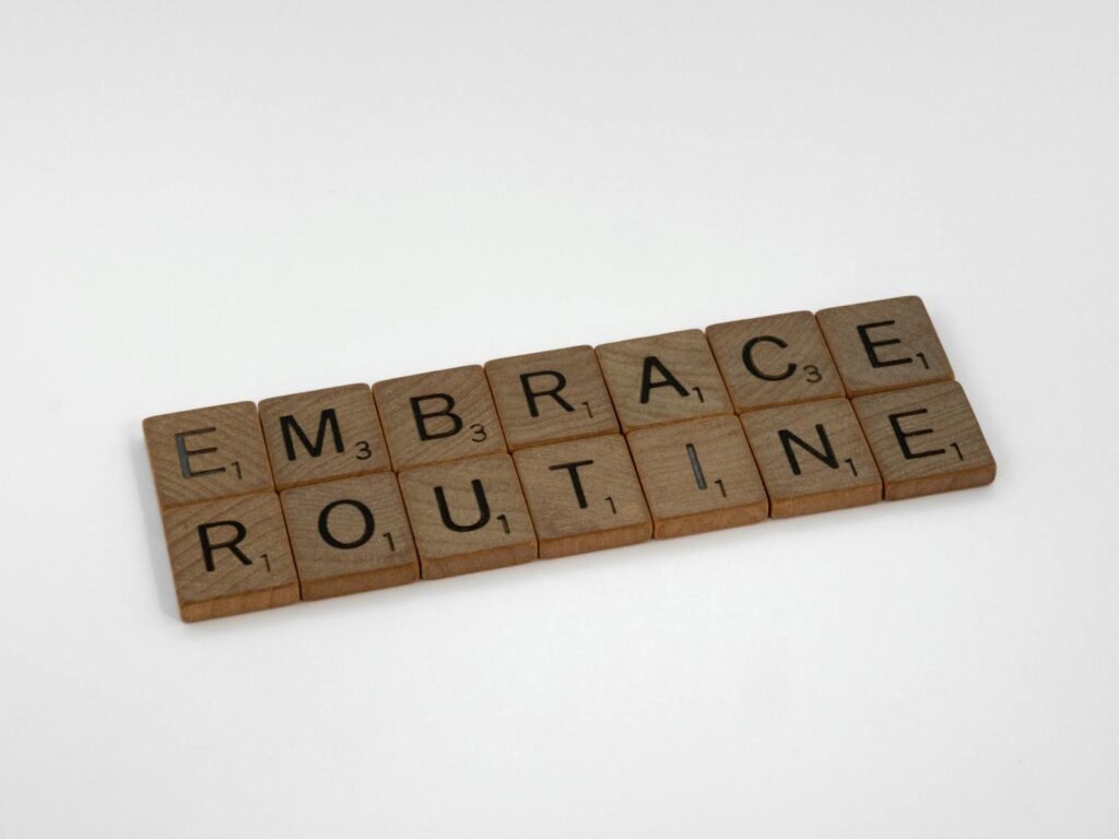 Wooden Scrabble tiles spelling 'Embrace Routine' on a clean white background. Perfect for lifestyle and typography concepts.