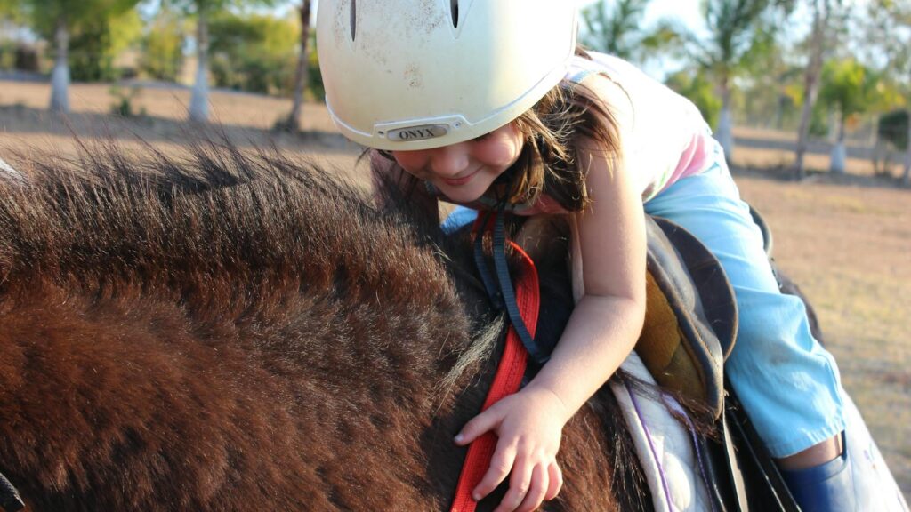 Young girl smiling while horseback riding with helmet outdoors in sunny Australia.