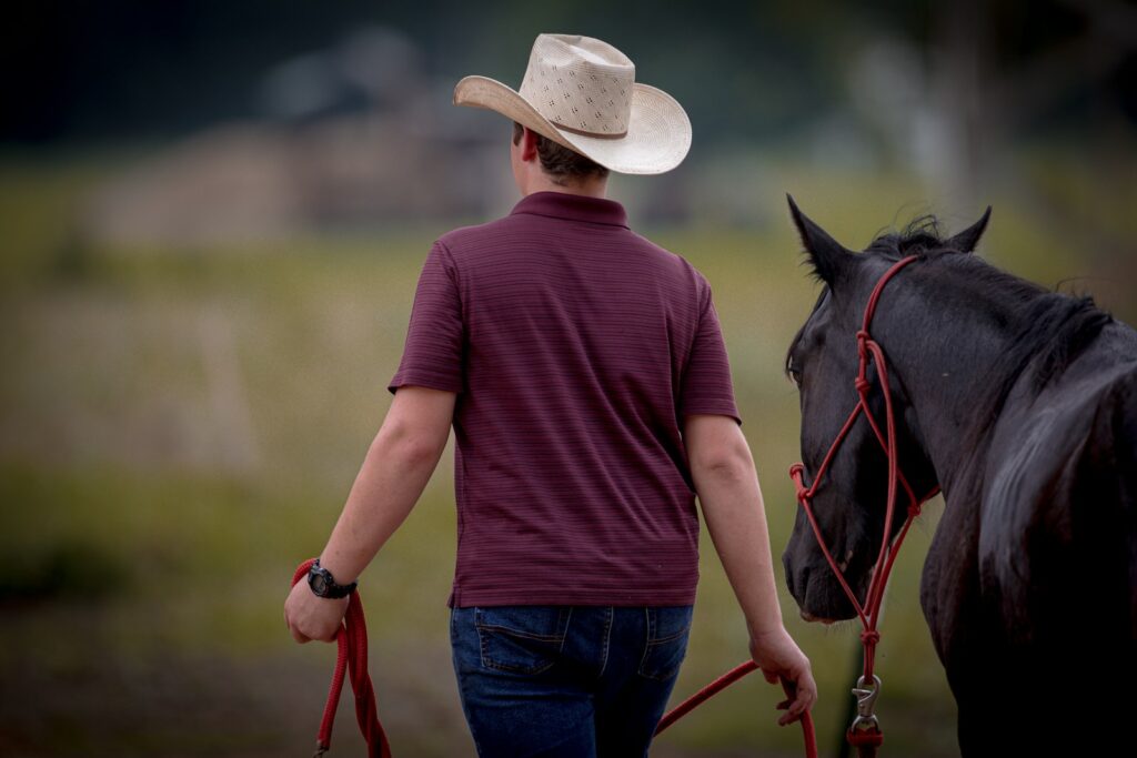 A man in a cowboy hat walking a horse