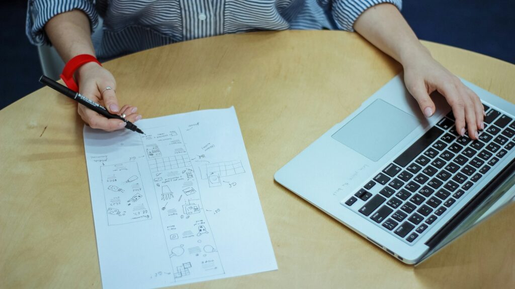 woman sketch on piece of paper while using laptop