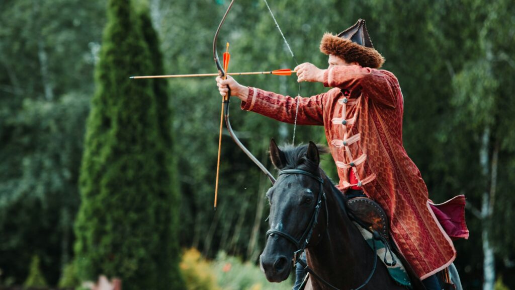 a man riding on black horse holding brown compound bow