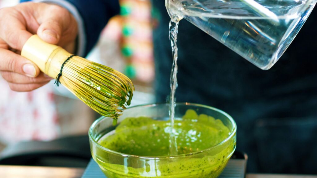 person pouring water into green sauce