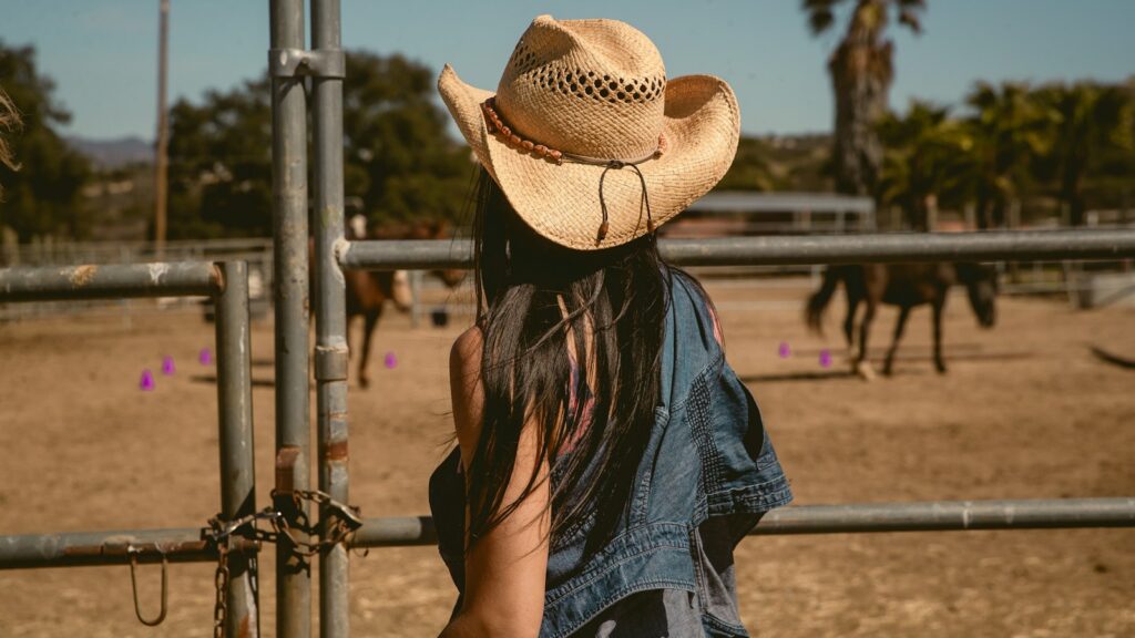 Cowgirl watches horses in a sunny corral.