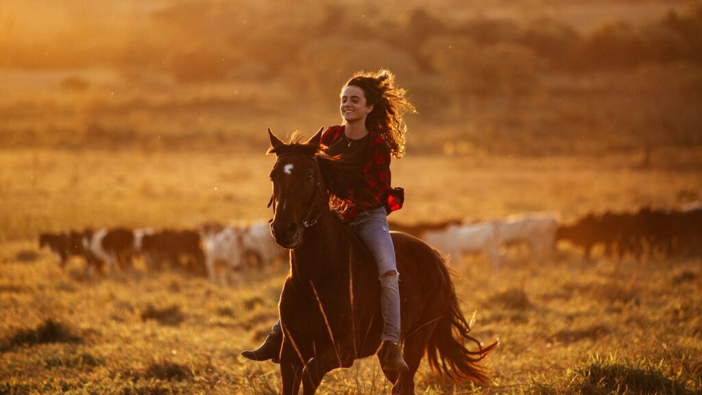 woman in red long sleeve shirt riding brown horse during daytime