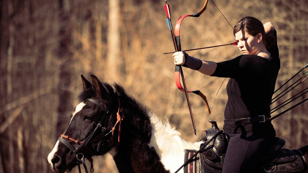 a woman riding on the back of a horse holding a bow and arrow