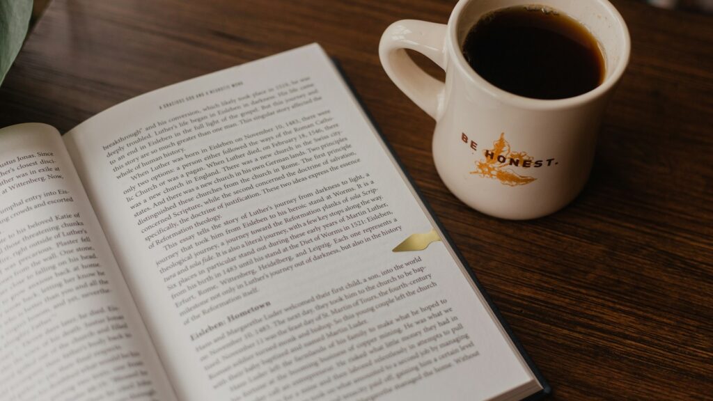 white book beside white ceramic mug on brown wooden table
