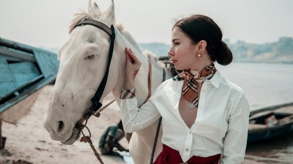 woman in white button up shirt standing beside white horse during daytime