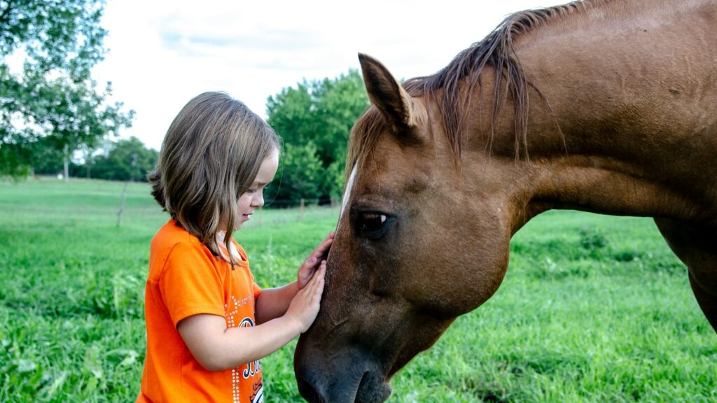 girl in orange t-shirt standing beside brown horse during daytime