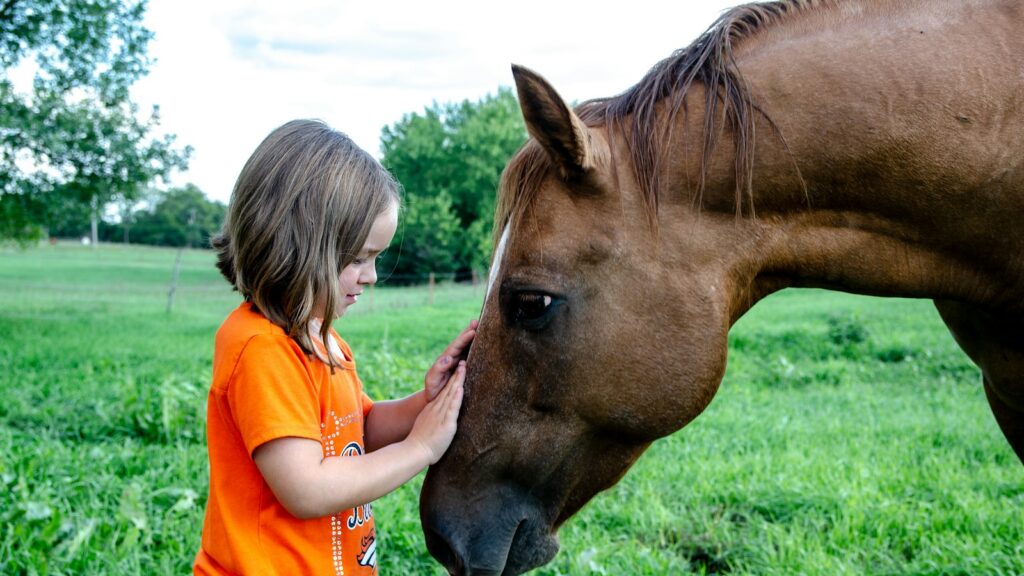 girl in orange t-shirt standing beside brown horse during daytime
