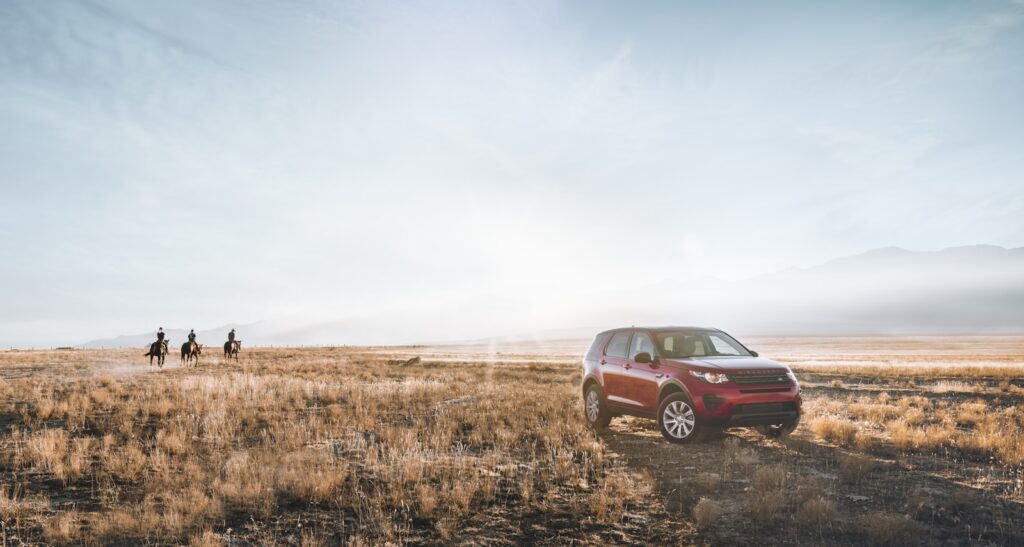 Red SUV on field and three person riding horse