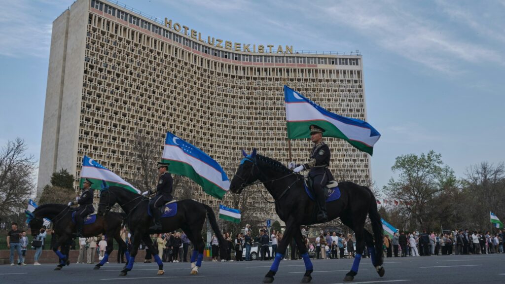 Horseback riders parade with flags near a large building.