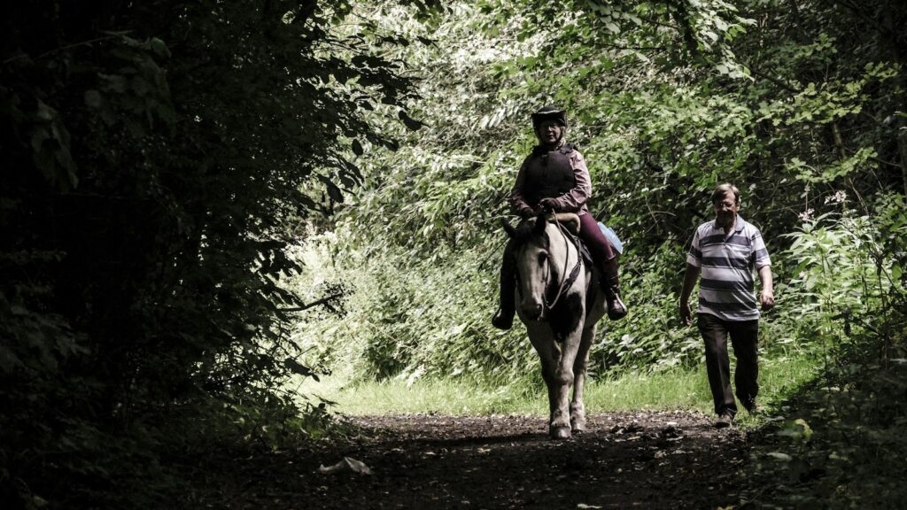 person riding on horse beside man walking on forest