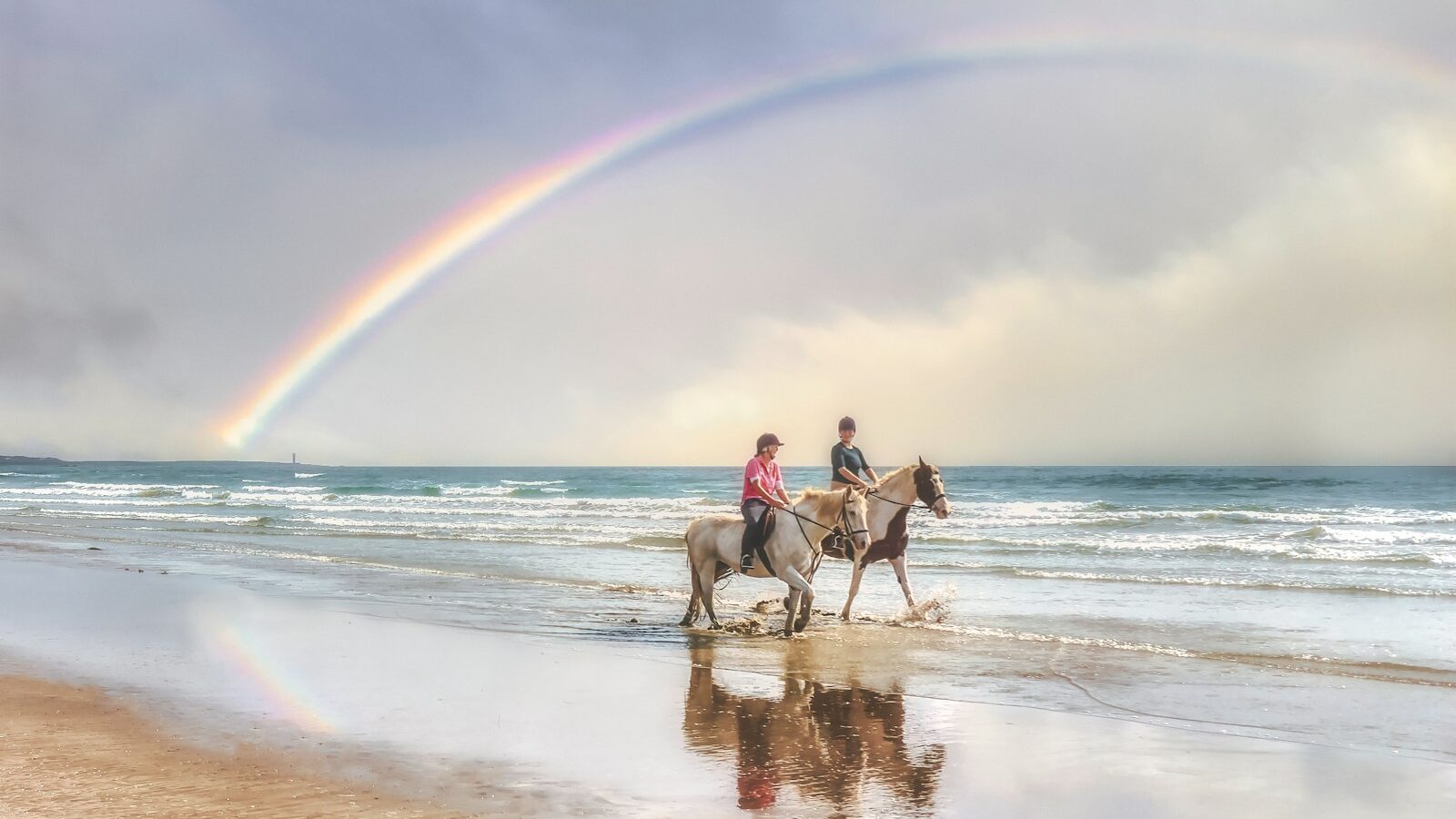 2 men riding horses on beach during daytime
