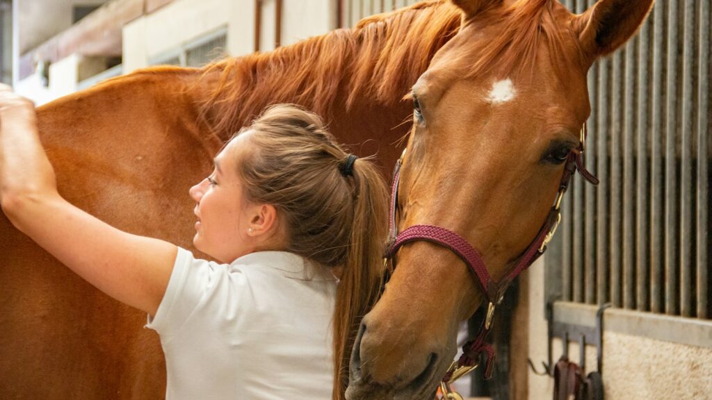 woman in white crew neck t-shirt standing beside brown horse during daytime