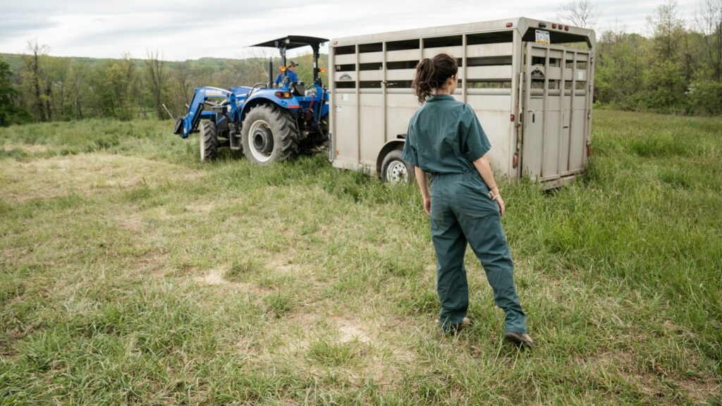 man in blue denim jeans standing beside a blue tractor during daytime