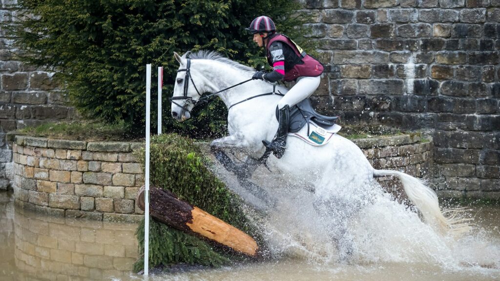 man riding on horse jumping over hedge
