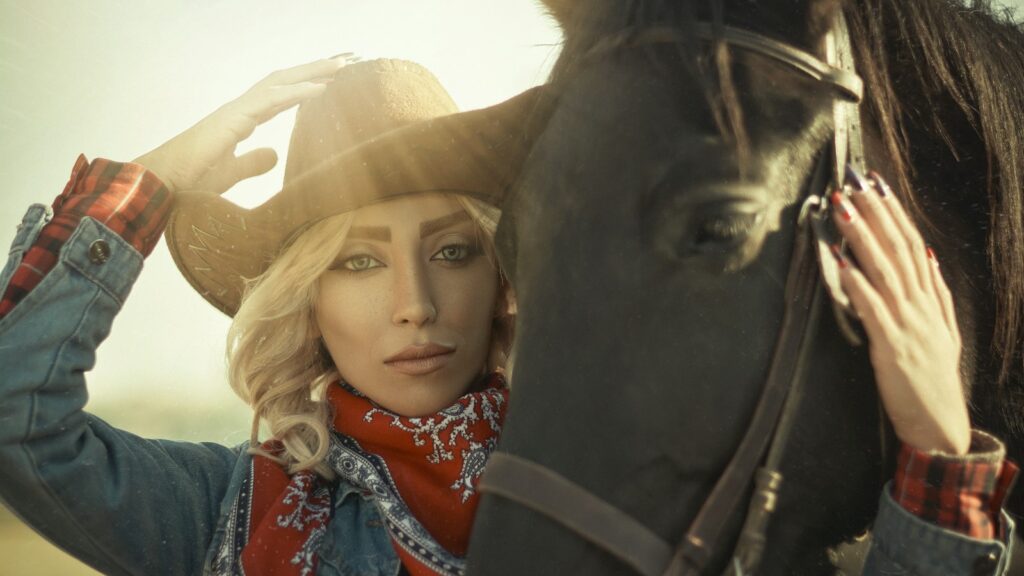 woman in blue denim jacket wearing brown cowboy hat beside black horse during daytime