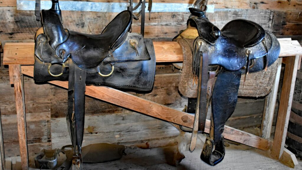 a couple of horse saddles sitting on top of a wooden bench