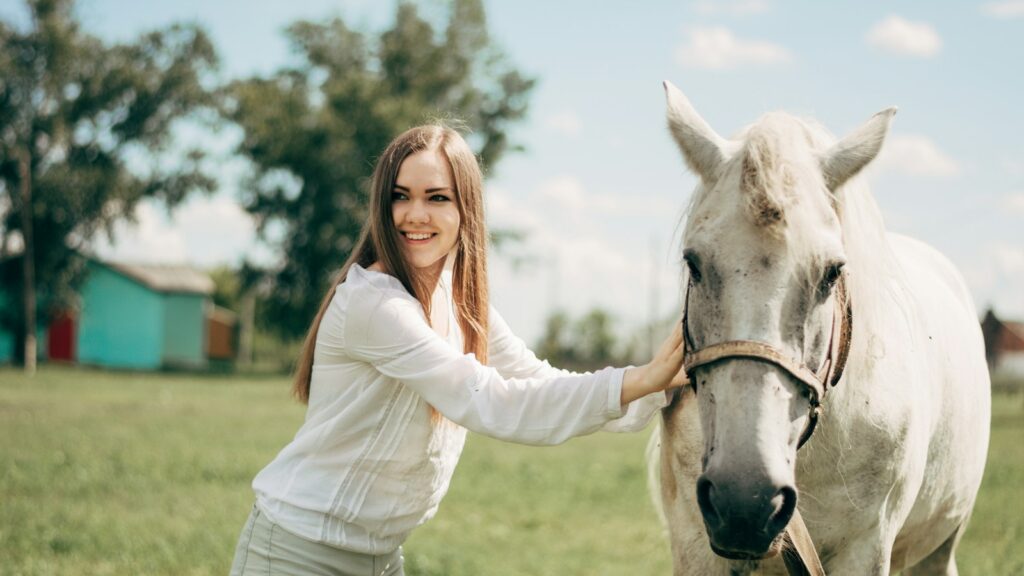 woman in white long sleeve shirt riding white horse during daytime