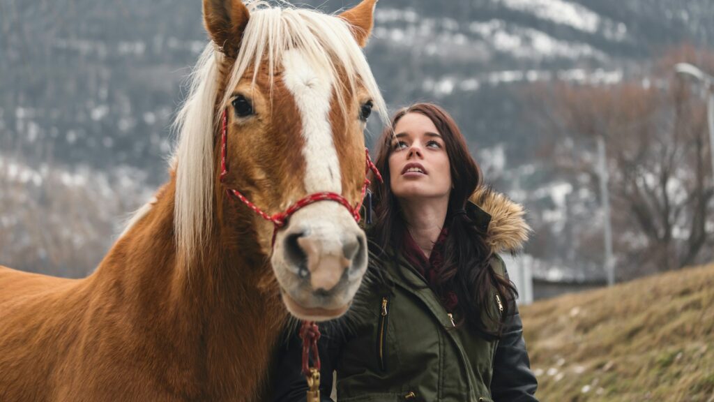 woman in green parka jacket standing beside brown horse