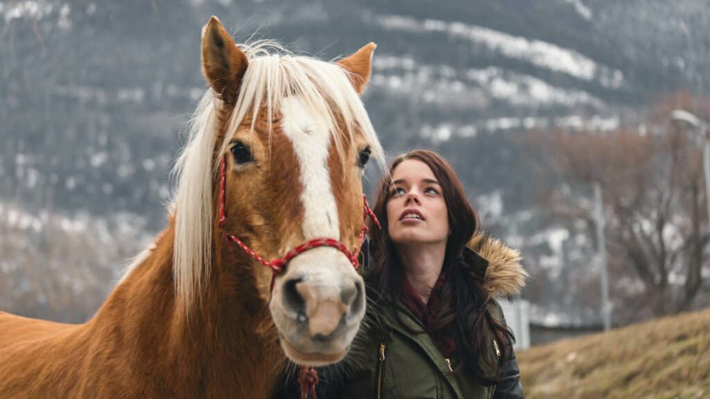 woman in green parka jacket standing beside brown horse