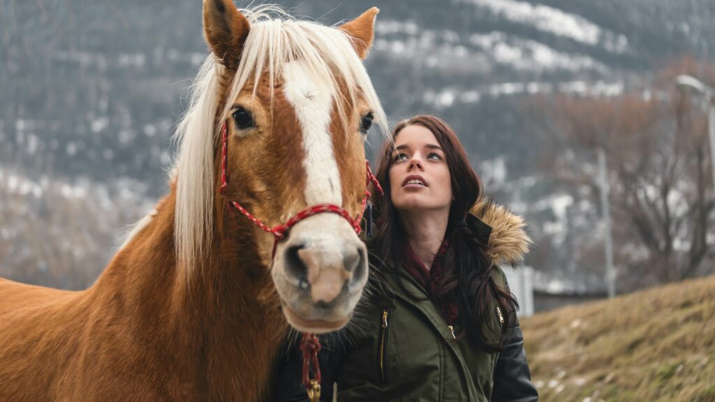 woman in green parka jacket standing beside brown horse