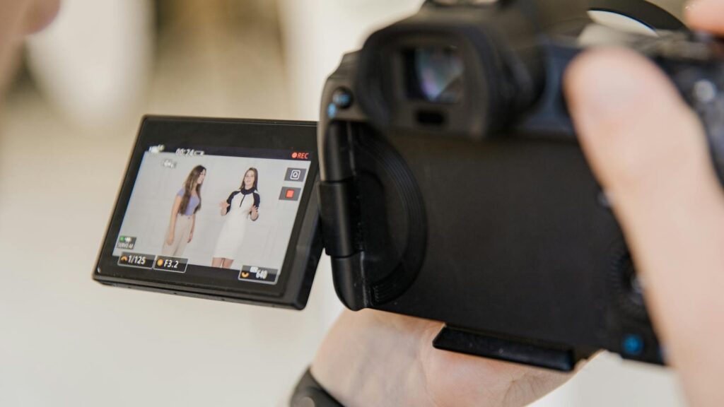 Close-up of a digital camera screen capturing two women recording content indoors.