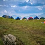 Picturesque mountain campsite with colorful tents and grazing horses under a dramatic sky.