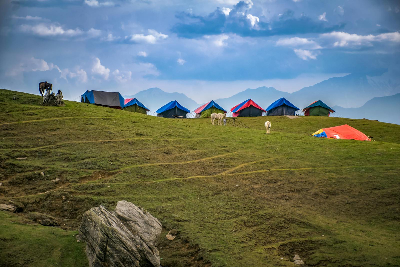 Picturesque mountain campsite with colorful tents and grazing horses under a dramatic sky.