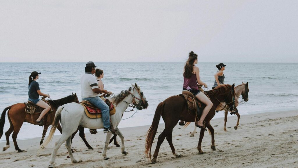 Group of people enjoying horseback riding along Bucerías beach, Mexico, against ocean waves.