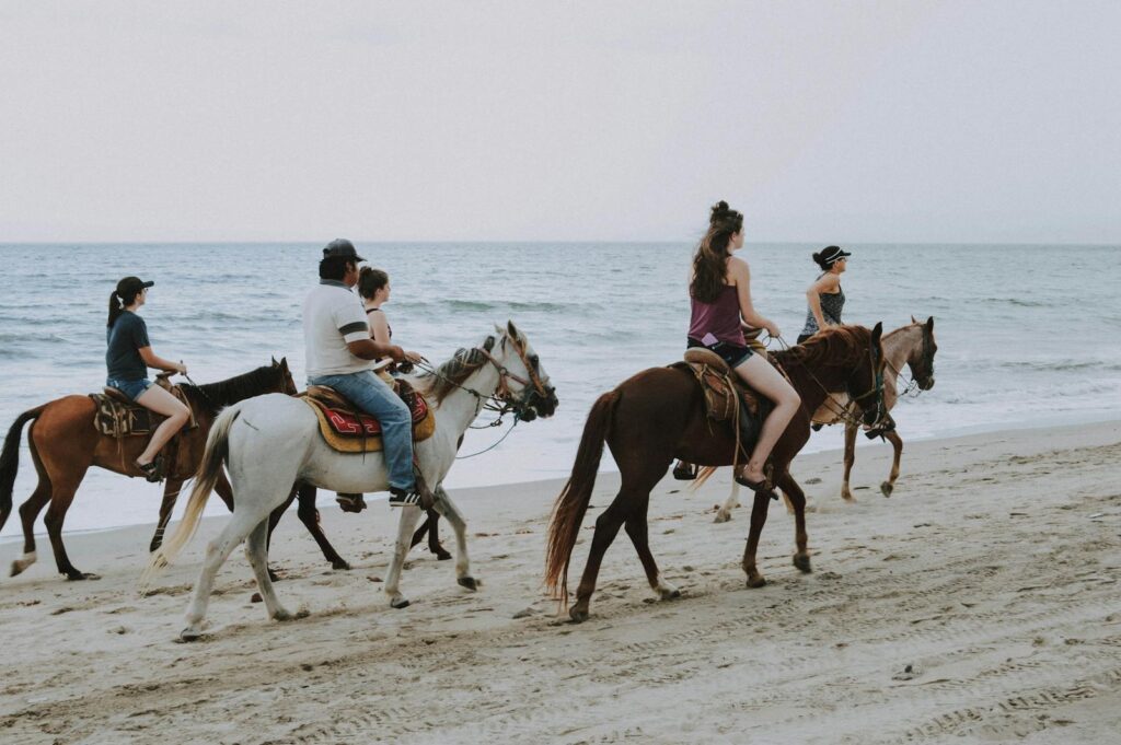 Group of people enjoying horseback riding along Bucerías beach, Mexico, against ocean waves.