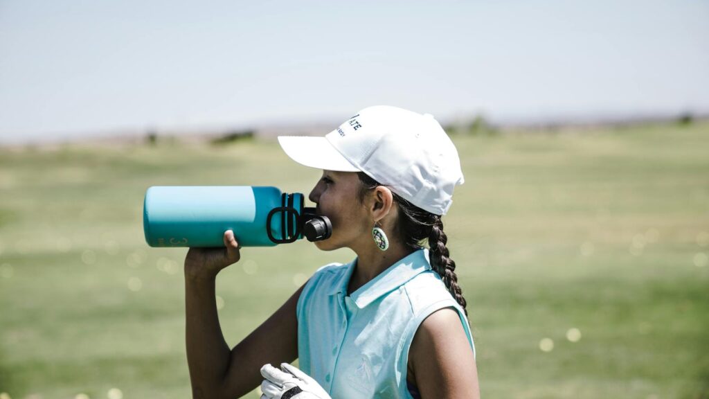 Woman golfer taking a break to hydrate on a sunny day in a field.