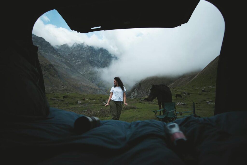 A woman enjoys camping with a horse in a foggy mountain landscape, view from tent.