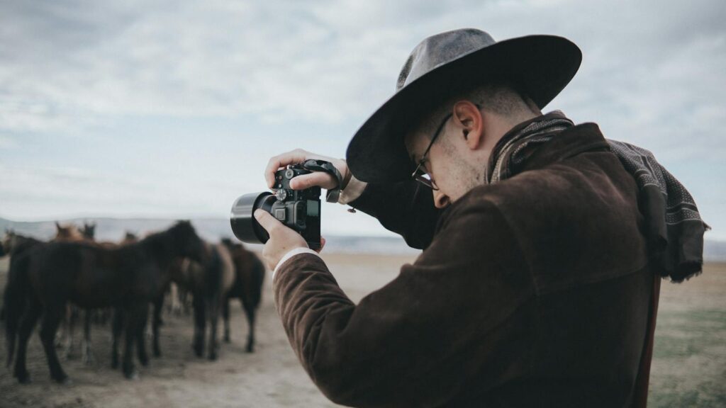 A man photographs a wild horse herd in a natural outdoor setting, emphasizing adventure.