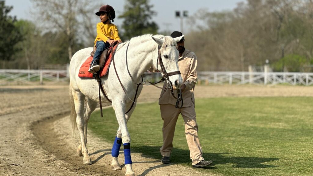 A young child enjoys a horseback ride with guidance in a serene Islamabad park setting.
