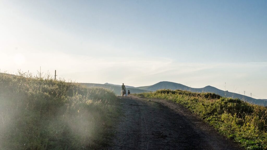 A tranquil scene of people walking on a rural path with hills in the background.