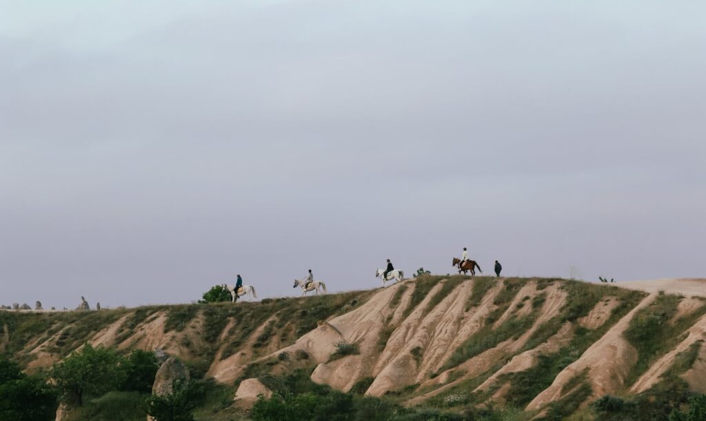 A stunning view of horse riders traversing hilltops under an expansive sky at twilight.