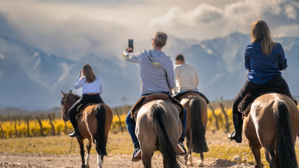 Four adults horseback riding in a scenic field with mountains in the background.