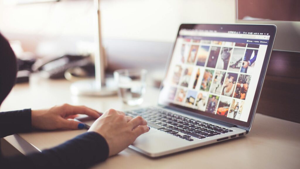 Close-up of hands typing on a laptop with an image gallery open on the screen.