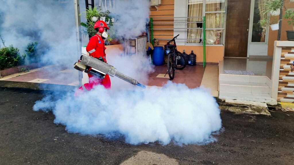 Pest control specialist using a smoke machine to fumigate outside a house.
