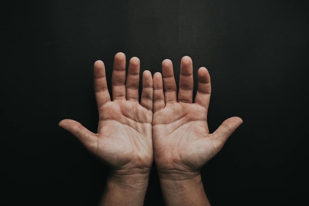 A pair of upturned hands displayed against a dark background, showcasing skin texture.
