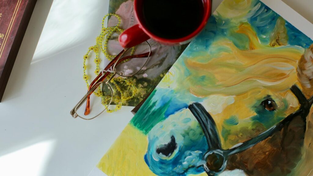 A vibrant still life featuring a coffee cup, colorful horse painting, and eyeglasses on a table.