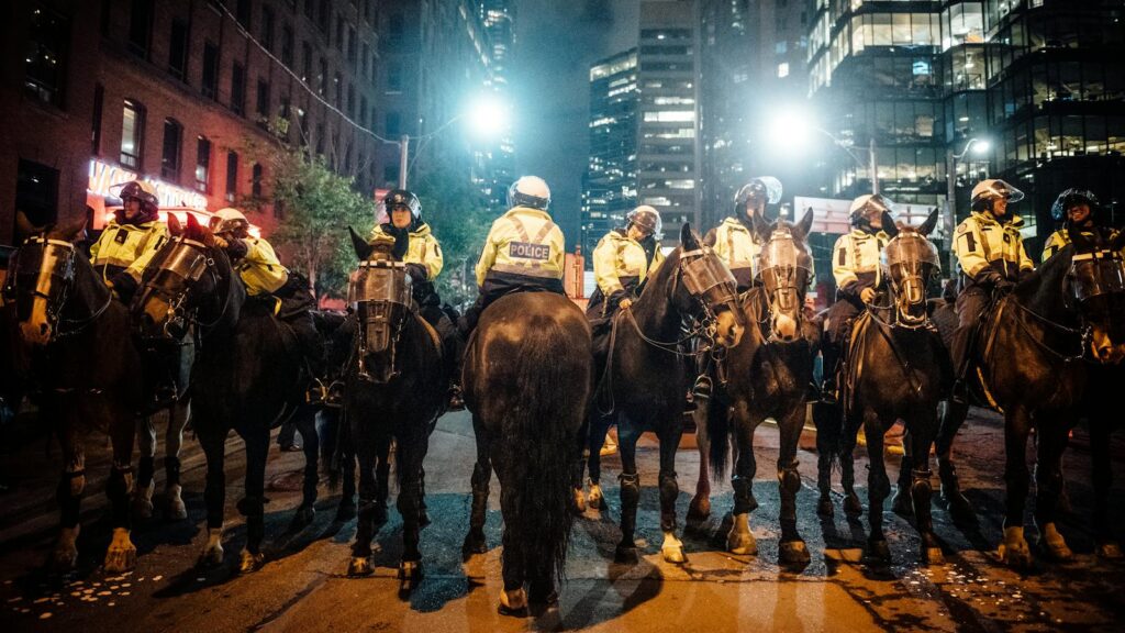 A line of mounted police officers in the city during a nighttime protest, maintaining order.