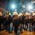 A line of mounted police officers in the city during a nighttime protest, maintaining order.