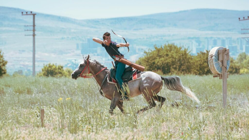 A horseback archer practicing in a lush green field in Konya, Türkiye.