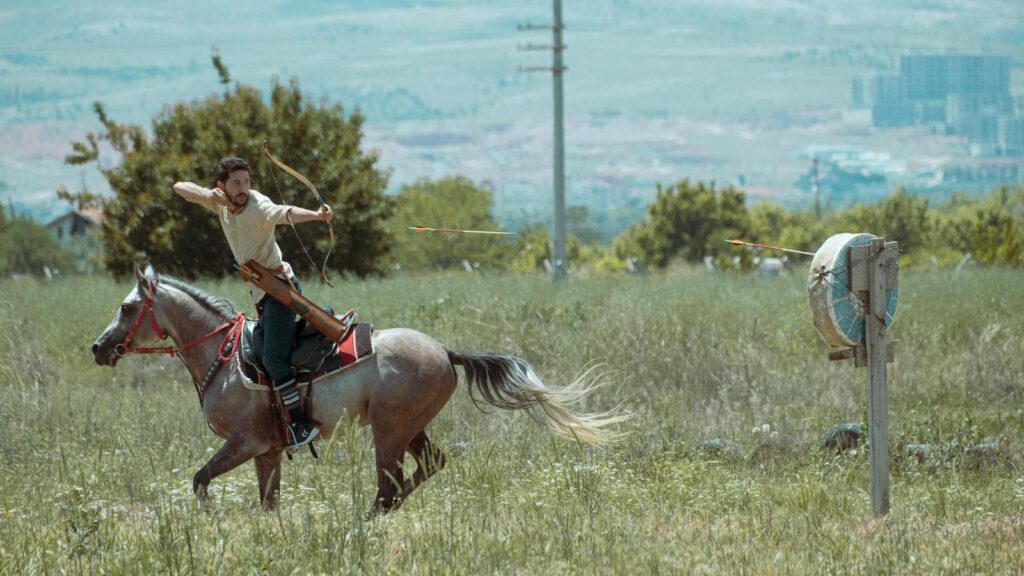 Dynamic scene of a mounted archer practicing in a field with a clear mountain backdrop in Konya, Türkiye. Captured outdoors in daylight.